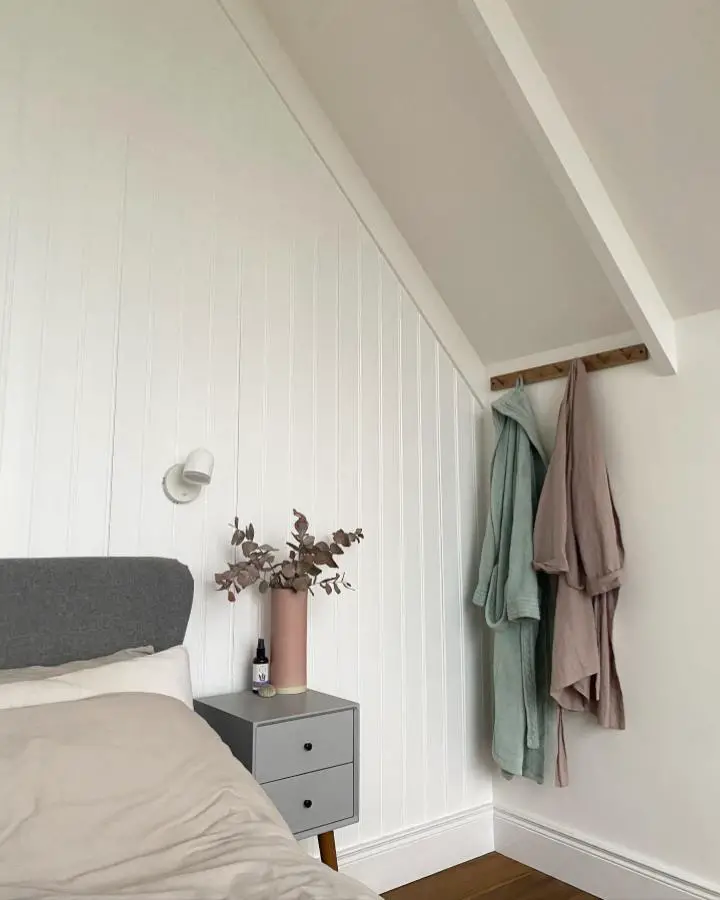 White paneled attic bedroom showcasing scandi bedroom ideas with exposed beams and neutral linens.
