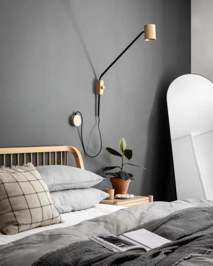 Minimalist bedroom setup from @liron_cohen_maguri featuring natural wood headboard and adjustable reading light.