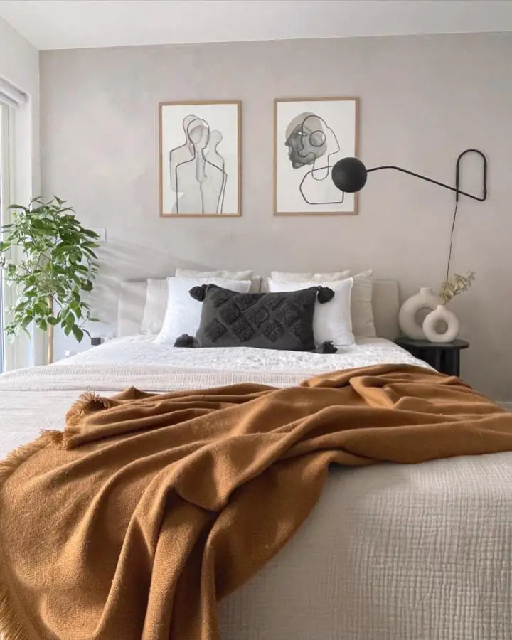 Warm ochre knitted throw from @claphamhome draped over white bedding with abstract art above headboard.