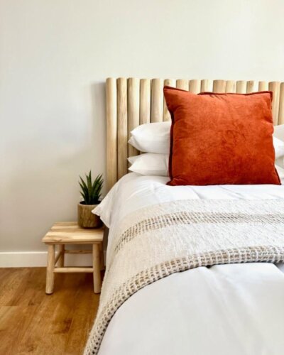 Natural wood slat headboard from @neverfullyfinished. Burnt orange pillow adds warmth to neutral bedding.
