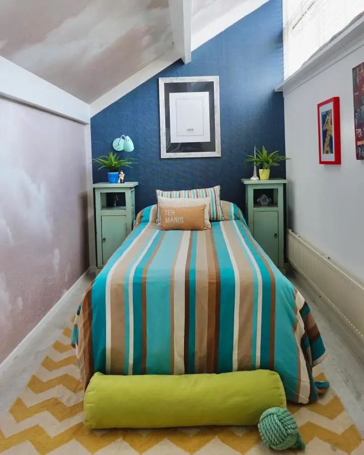 Cozy attic bedroom from @ajourneyofcolourandstyle featuring built-in green nightstand cabinets and colorful striped bedding.