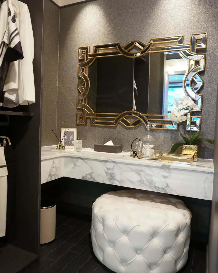 Geometric gold mirror vanity setup from @dnosdesign featuring small dressing room ideas with marble countertop and tufted storage ottoman.