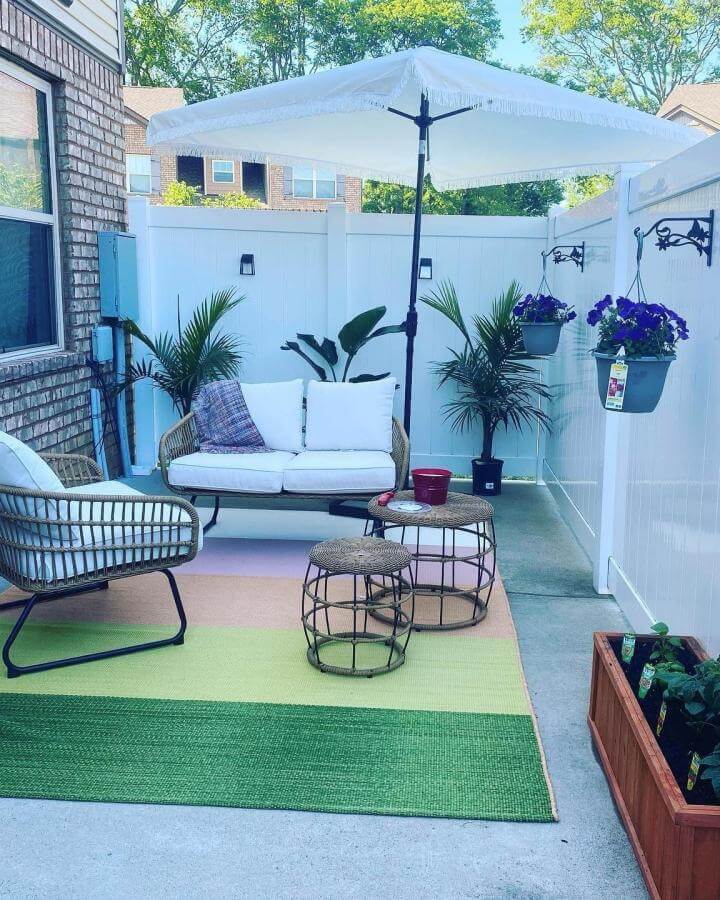 Natural rattan furniture and bright cushions on a small patio with green plants and hanging flower pots from @minimal_mara small patio ideas. Cozy and fresh outdoor space.