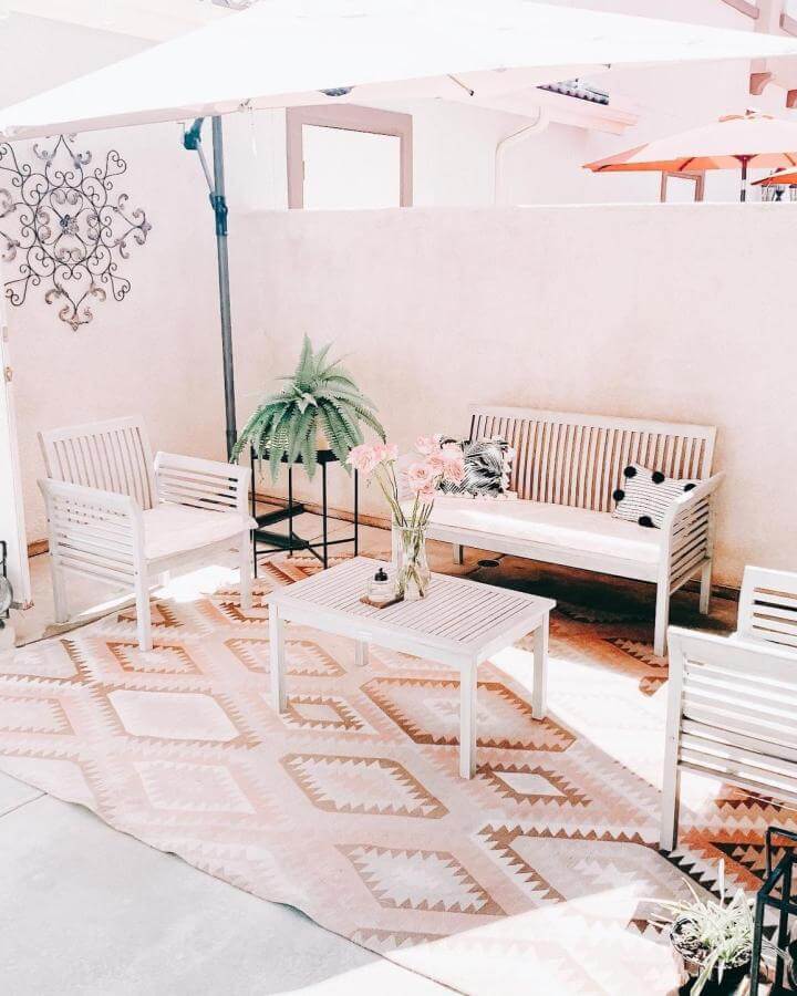 White wood patio furniture and peach patterned rug from @homesweetgold_ create a bright and inviting outdoor seating area.