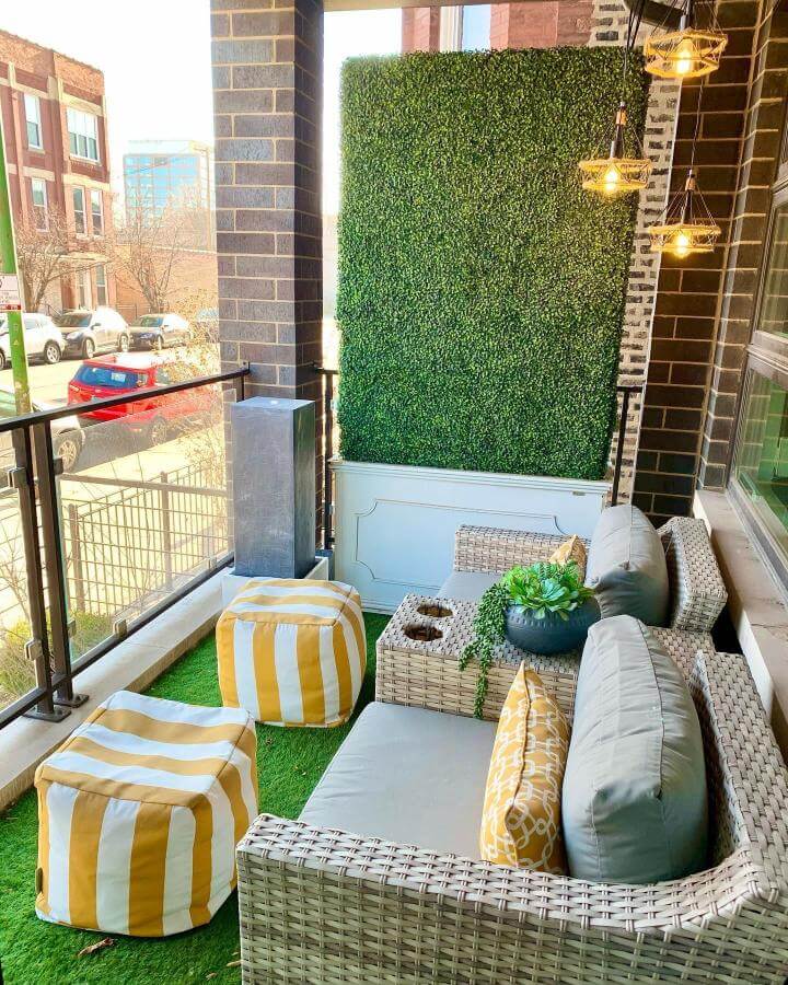 Green faux boxwood wall with woven rattan sofa and yellow striped poufs on small urban patio by @homeoncarpenterstreet bright and inviting space.