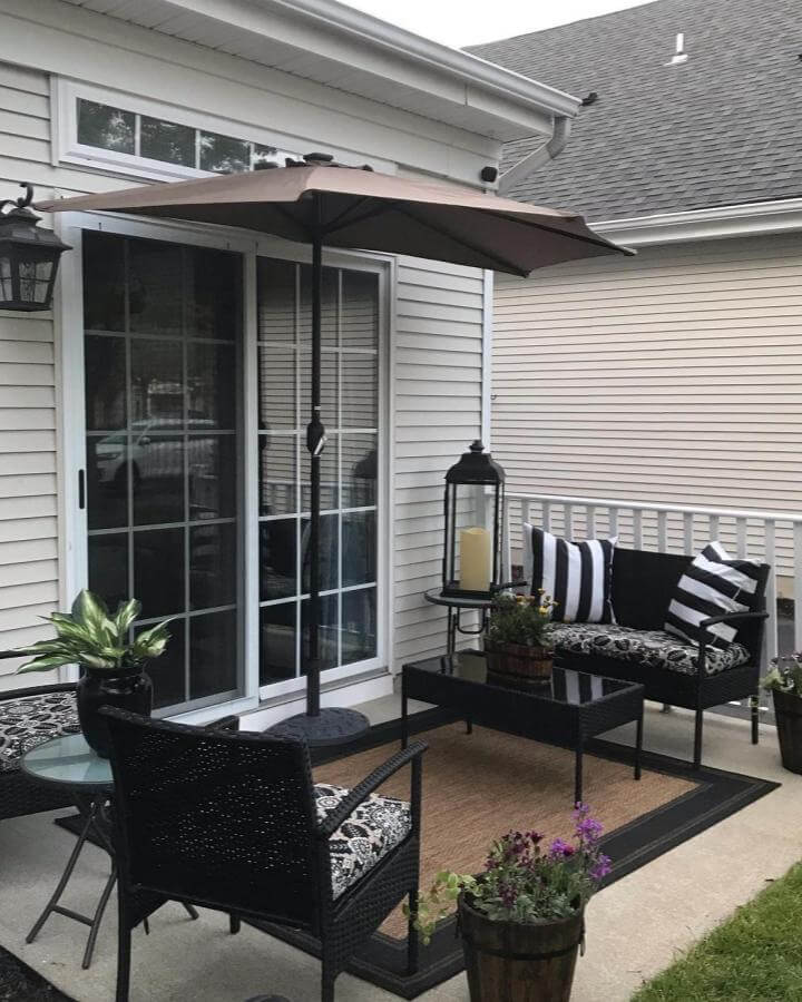 Black wicker seating with patterned cushions on a small patio from @ourmanorhome featuring umbrella and plants perfect for small patio ideas.