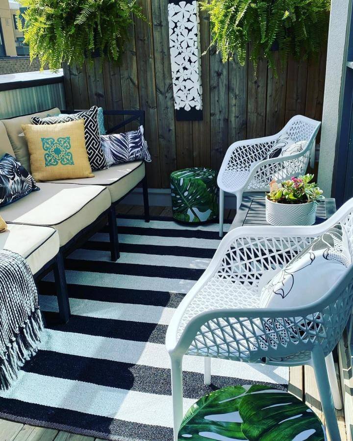 White lattice plastic chairs and beige cushioned black metal sofa with tropical pillows on striped black and white rug outdoor patio by @nia_da_design_inspirations. Cozy compact seating with bold patterns and leafy accents.