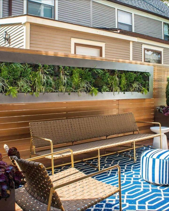 Woven chair and bench patio seating with vertical garden and blue patterned rug from @ieedesigns. Cozy outdoor living space.