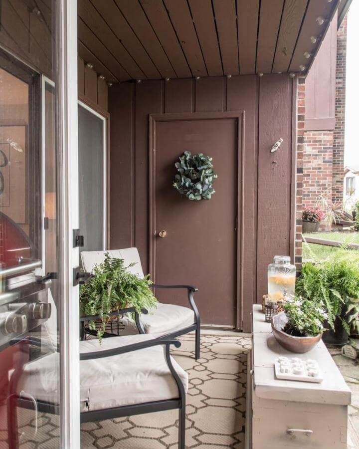 Brown cozy patio with cushioned seating and ferns by @nzdesign19. Small outdoor space with patterned rug and natural accents.