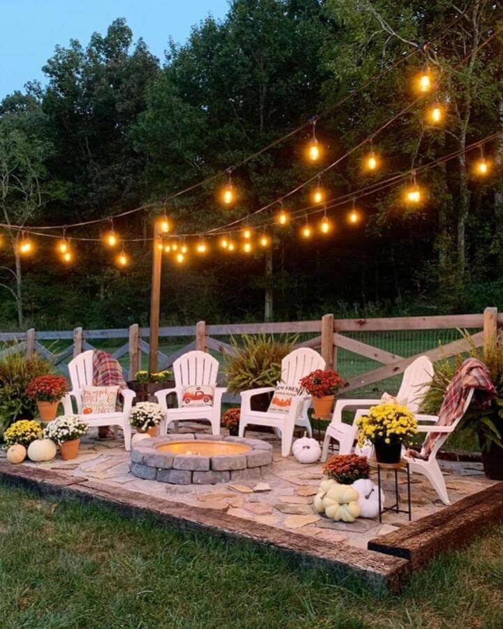 White Adirondack chairs and stone fire pit on a cozy patio with string lights and autumnal decor by @myslice_of_heaven creating a warm outdoor space.