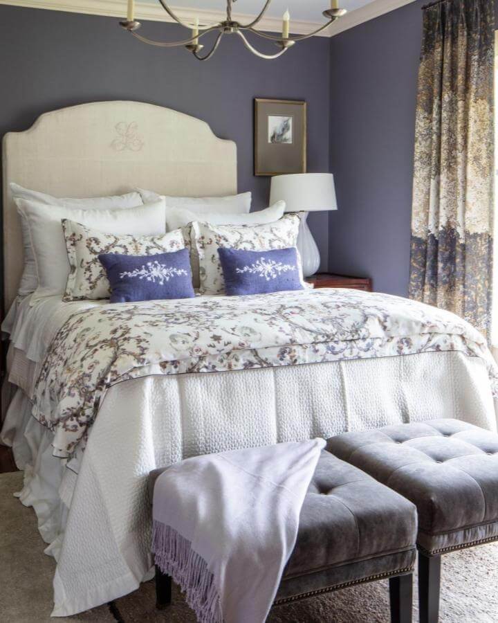 Soft lavender and cream bedroom with patterned bedding and velvet benches from @leighjonesinteriordesign. Cozy, layered textures create a serene space.