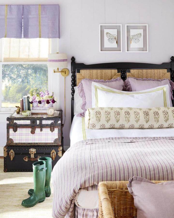 Soft lavender tones and natural rattan headboard in a cozy bedroom from @countrylivingmag with vintage suitcase bedside.
