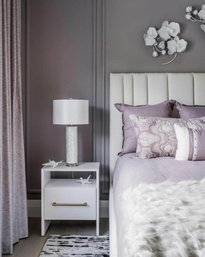 Soft lavender bedding and pillows with cream headboard and white nightstand in a cozy bedroom by @dwestfl. Plush textures and muted tones create calm.