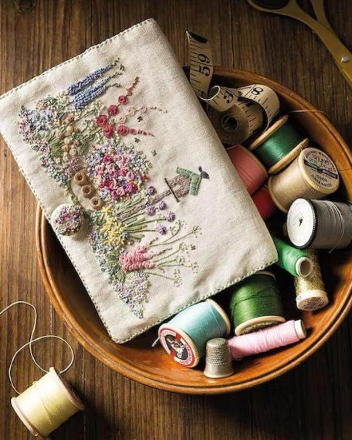 Pastel floral embroidery on linen with vintage thread spools for spring crafts for adults by Lorna Bateman. Detailed garden stitching and soft textures.