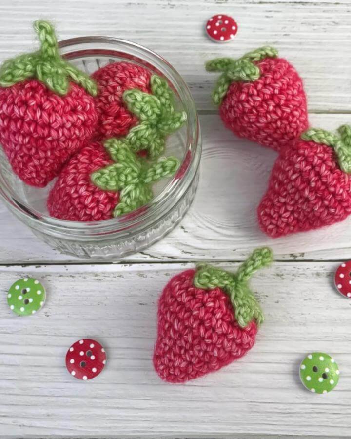 Bright red and green crocheted strawberries on white wood background from @knitcrochetcreate spring crafts for adults small handmade decor