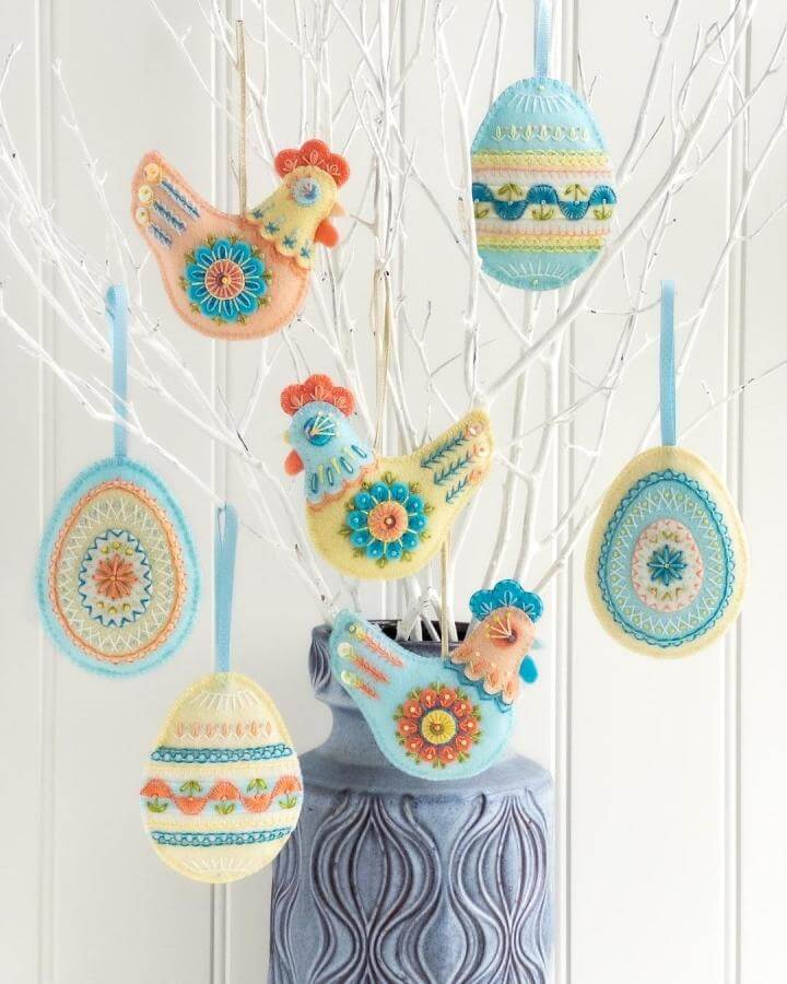 Light pastel felt Easter egg and chicken ornaments hanging on white branches for spring crafts for adults by @thehoopinhand with embroidery details.