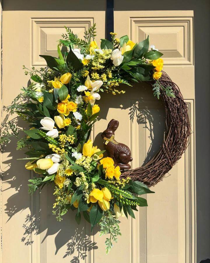 Yellow and white floral grapevine wreath with greenery and chocolate bunny on door from @posiesandpetals.co spring crafts for adults.