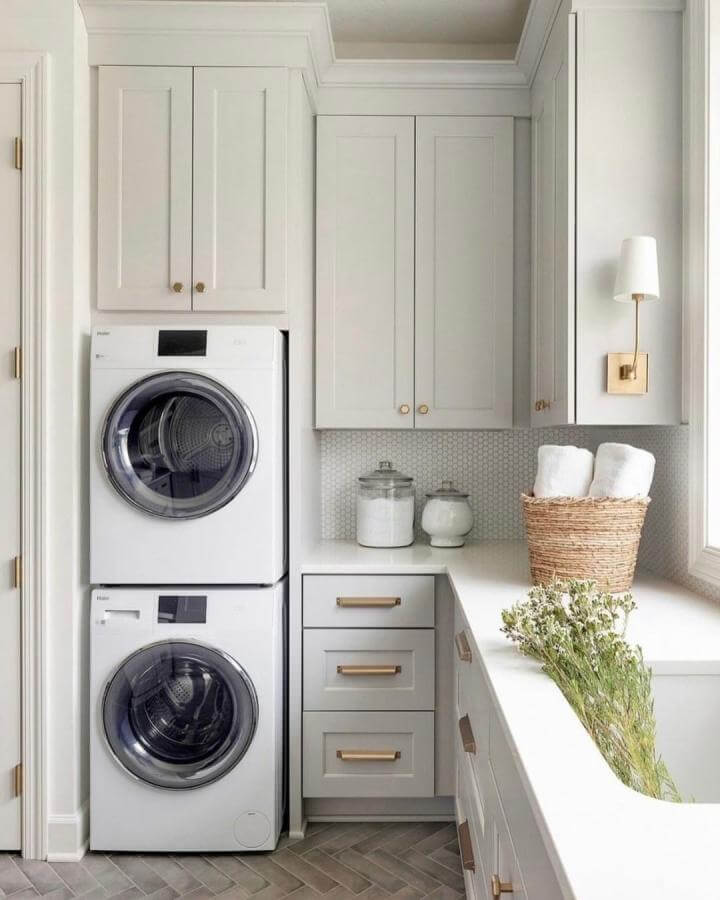 Soft gray shaker cabinet laundry space from @ohara_interiors with brass accents and natural decor around compact laundry machines.