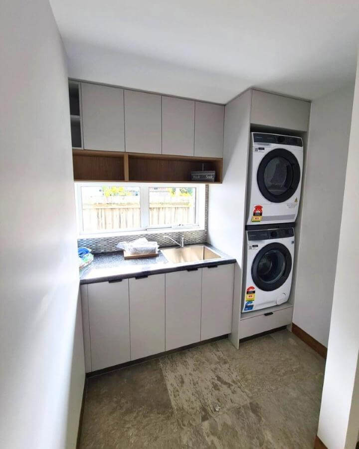 Light gray and wood laundry room unit from @industry_kitchens_joinery featuring stacked appliances and sleek hidden storage.