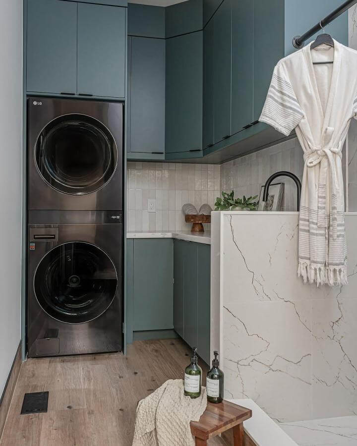 Soft blue cabinetry laundry nook from @sparrowlaneinteriors with stacked washer dryer and modern black hardware details.