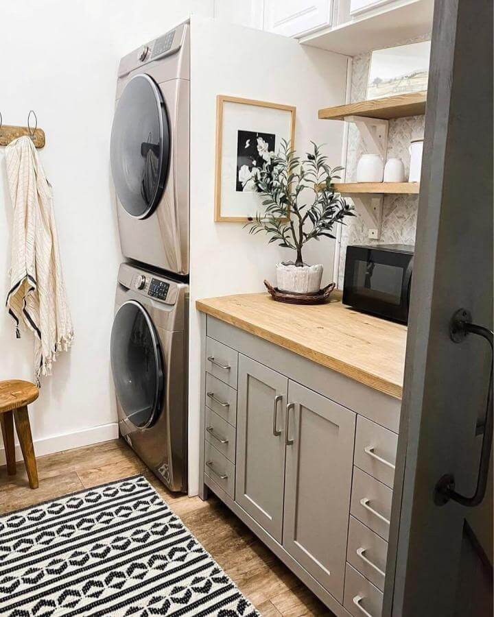 Natural wood countertop and soft gray cabinetry laundry nook from @gina.keilen with open shelves and patterned tile backsplash.
