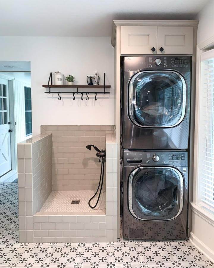 Light beige tiled laundry nook with modern black fixtures and patterned floor tiles from @edenandgraydesignbuild. Functional stacked washer and dryer setup.