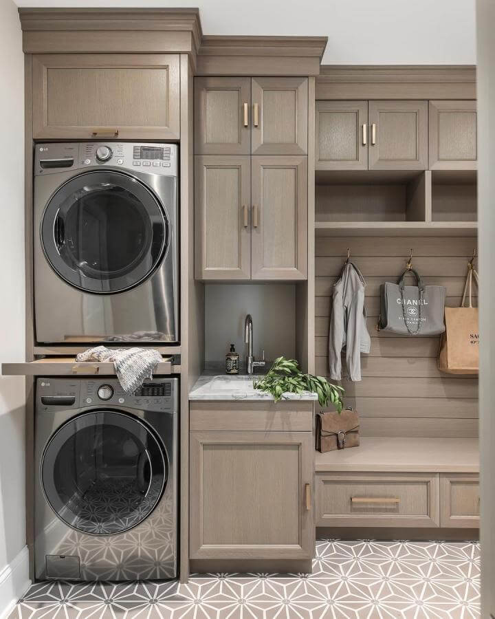 Neutral-toned laundry nook with built-in cabinetry and patterned tile by @amystormandco featuring stacked appliances and marble sink counter.