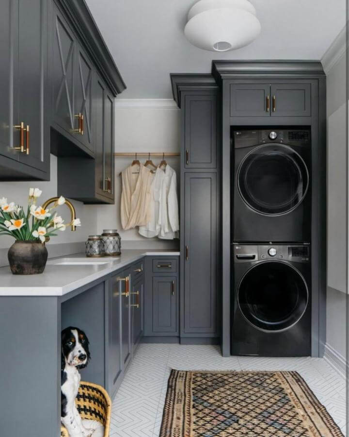 Dark gray cabinetry with gold hardware in stacked washer dryer laundry rooms from @margaretrajic. Cozy and stylish with patterned rug and hanging rod accents.