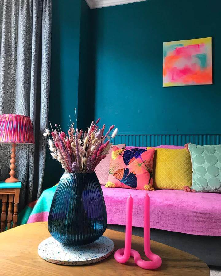 Teal painted living room wall with pink sofa and colorful cushions by @nia_does_diy Vibrant and playful cozy interior style.