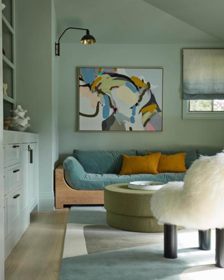 Teal velvet sofa with wooden frame from @jmorrisdesigner. Cozy living space with mustard pillows and abstract wall art.