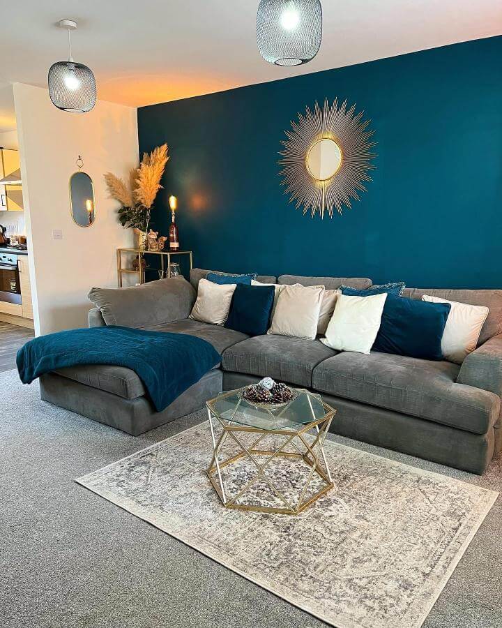 Teal accent wall and gray sectional from @home_on_birchfield_road showcase stylish teal living room ideas with gold and glass details.