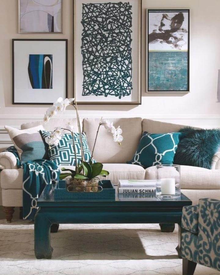 Teal patterned cushions and dark wood coffee table in elegant living room by @dbrainstudiosg with neutral sofa and abstract wall art.