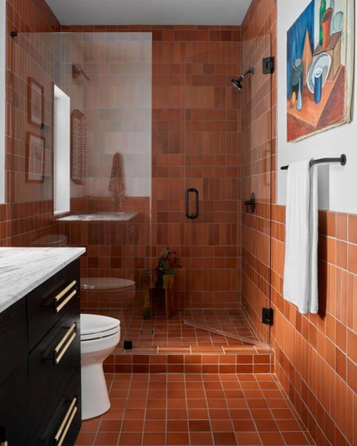 Terracotta tiled bathroom with glass shower door and black fixtures from @emilyfollowillphotographer. Warm earthy hues balanced by sleek dark accents.