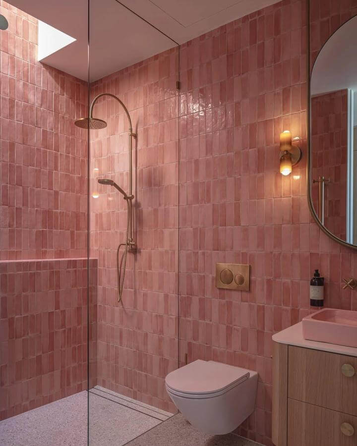 Glossy reddish-pink terracotta tiled bathroom wall with brass fixtures and glass shower from @cammurchisonphotography. Warm, textured, fresh design.