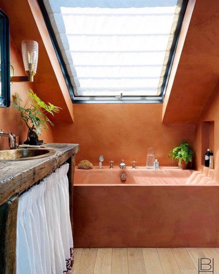 Terracotta bathroom ideas showing warm matte walls and tub with rustic wooden vanity and white curtain from @simonbrownphotography under natural skylight light.