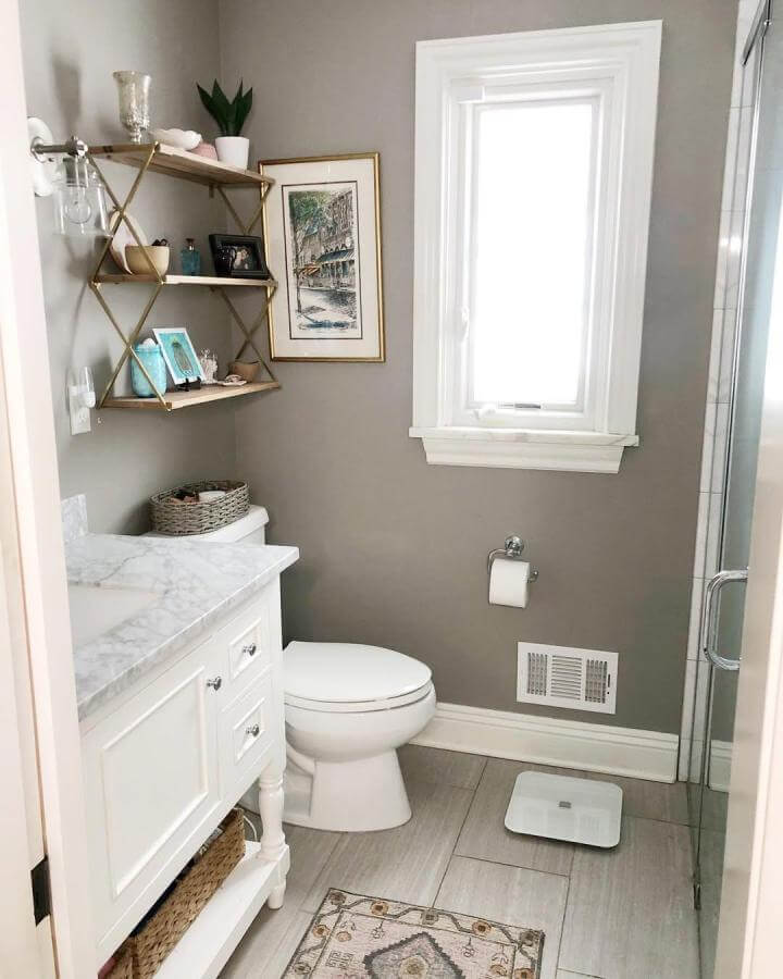 Light wood and gold metal open shelves from @22renovations. Bright tiny apartment bathroom ideas with stylish storage and soft gray walls.