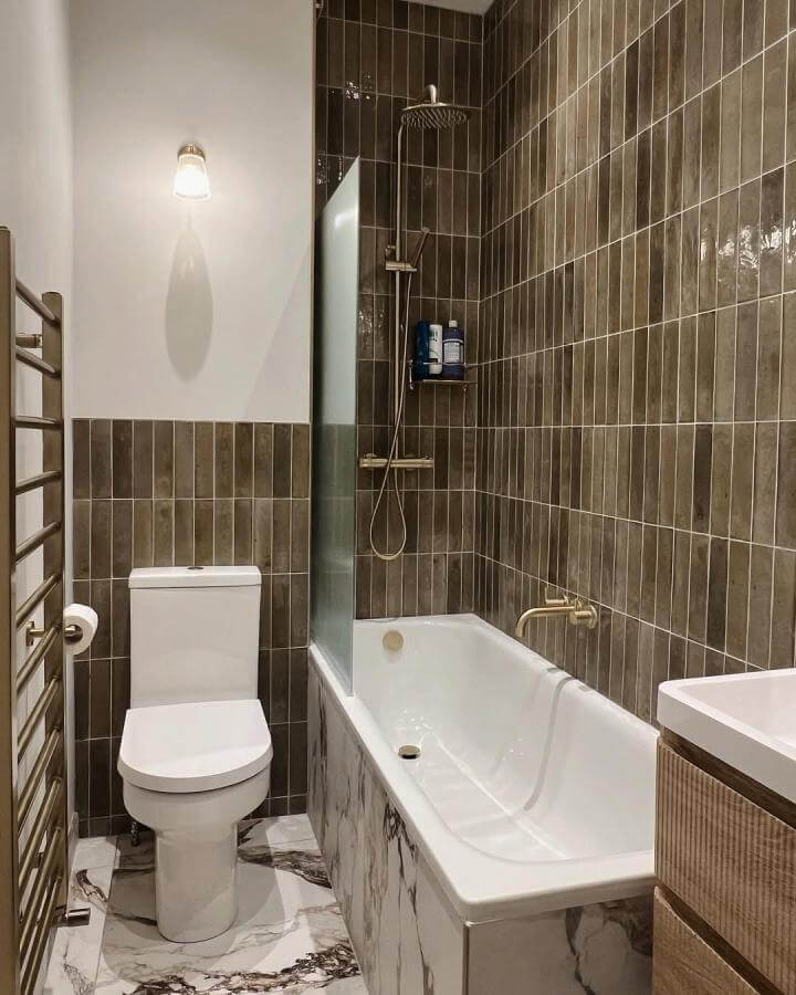 Brown vertical ceramic tiles bathroom with marble panel and brass fixtures from @steffy. Compact space with warm textures and modern details.