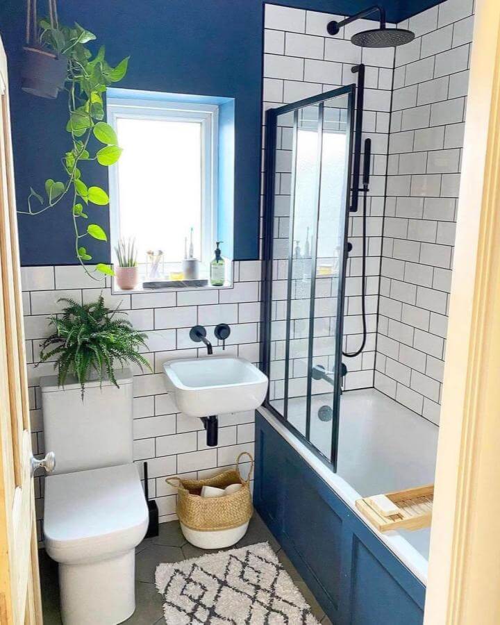 Navy blue paneled bathroom with white subway tiles and black fixtures from @blackbirdchateau featuring cozy woven basket and plants.