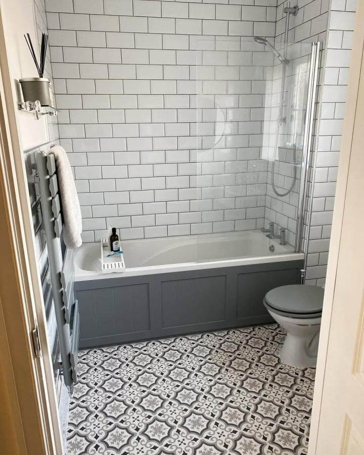 White subway tiled tiny apartment bathroom with grey bath panel and patterned floor from @alexandragater. Bright, classic tiny apartment bathroom ideas.