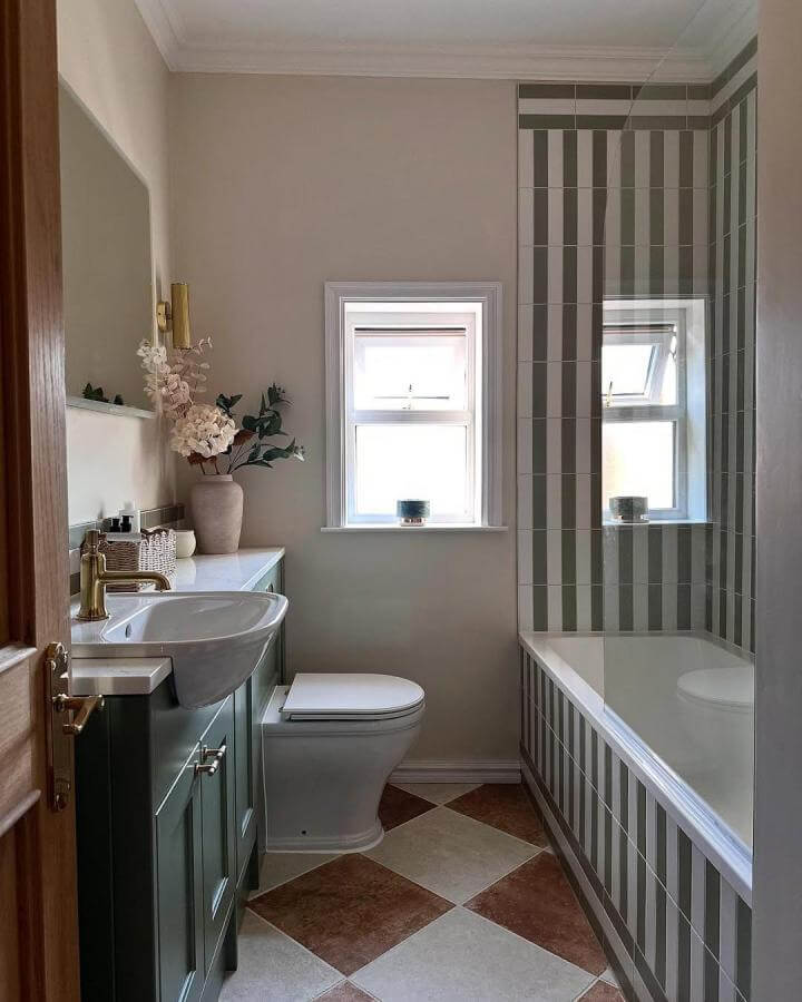 Muted green striped tile bathroom by @caropeony with brass accents and checkered floor maximizing small space charm.