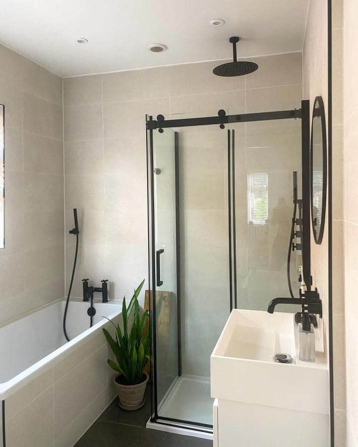 Black framed glass shower door and matte black fixtures in compact modern bathroom by @coffeepancakesdreams with green plant accent.