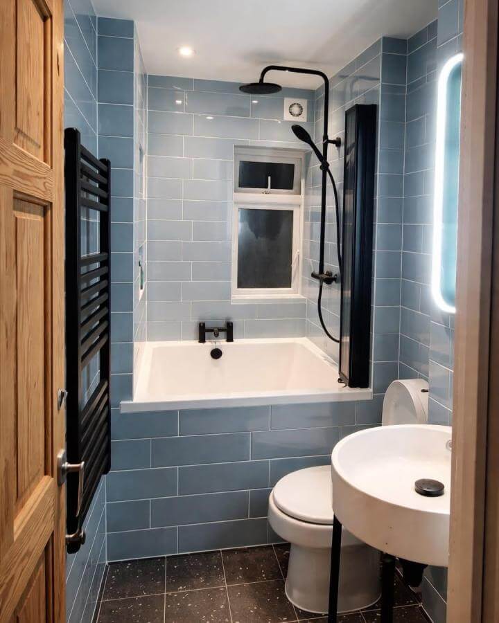 Blue subway tiled small bathroom with black shower fixture and heated towel rack from @girlmeetsnewyorkcity. Cozy, stylish compact space with natural light.