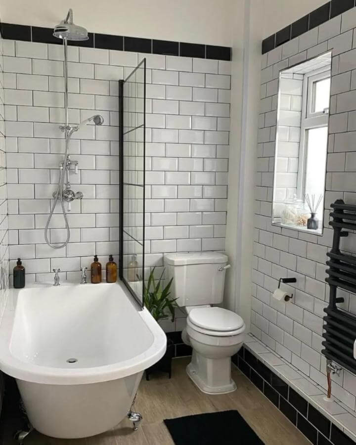 White subway tiled bathroom with black accents from @renovatingcouk. Small space with bathtub, glass shower screen, and rustic amber bottles.