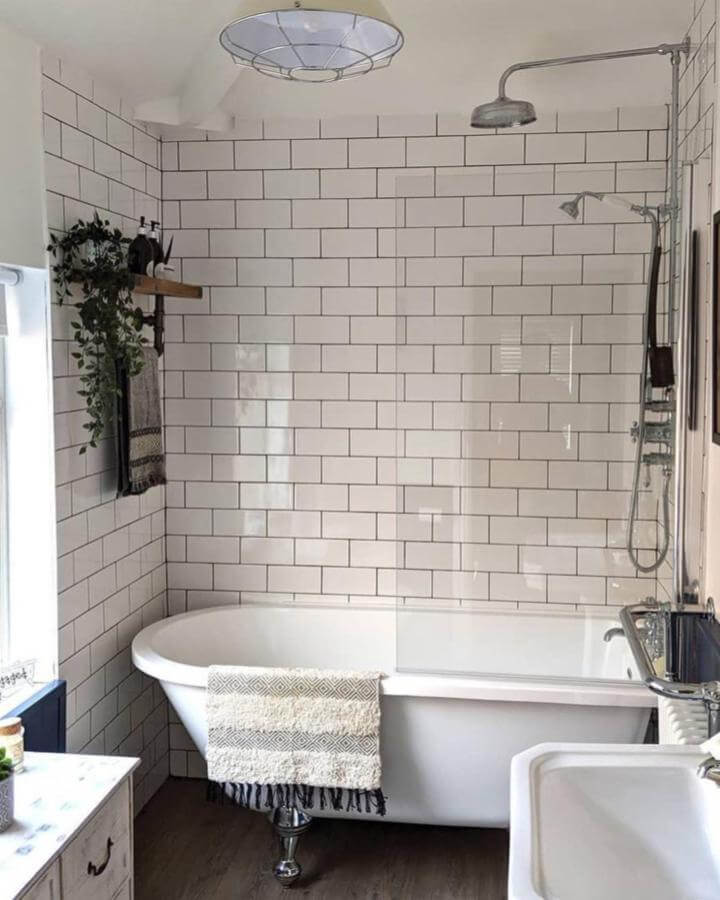White subway tile walled bathroom with clawfoot tub and natural wooden shelf from @j__lou__m. Victorian bathroom ideas with modern rustic touches.