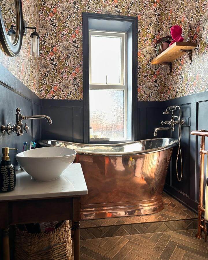 Copper freestanding bathtub in a Victorian bathroom with floral wallpaper and navy wainscoting by @lauren_oldcorn elegant mix of vintage and modern elements.
