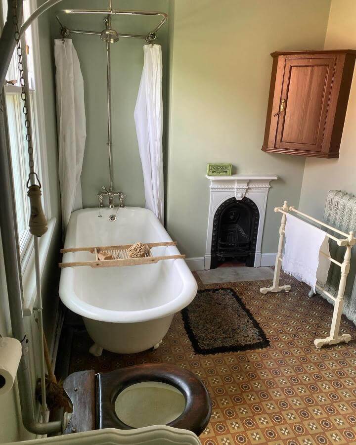 White clawfoot tub with silver shower rail and black fireplace in a victorian bathroom ideas room by @mrvictorian1900 showing vintage charm and patterned tile floor.