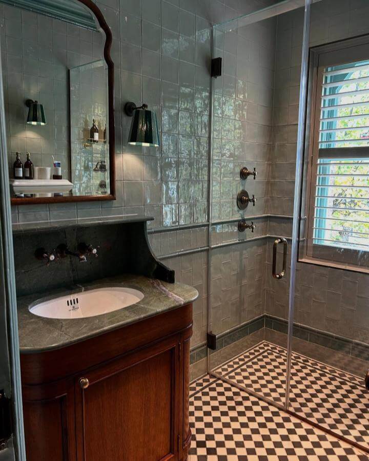 Checkerboard tiled bathroom floor with wooden vanity and green marble top Victorian bathroom ideas by @abbiedebunsen light reflecting glossy wall tiles and brass fixtures.