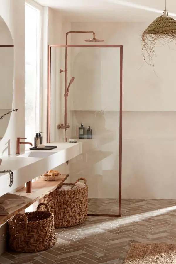Neutral bathroom with copper shower frame and woven storage baskets. Natural textures and warm metals create serene spa atmosphere.