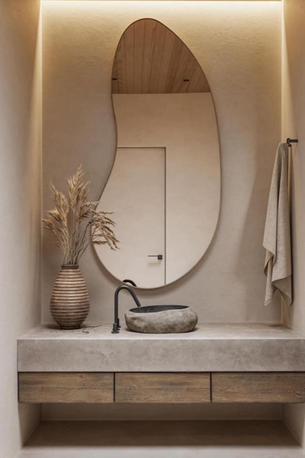 Natural stone vessel sink from @willoughby.and.bull. Organic bowl shape sits on concrete vanity with warm wood storage.