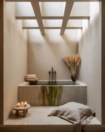 Natural stone bathtub sanctuary from @ancre.home showcasing wabi sabi bathroom ideas with wooden beams and skylights.